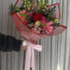 Handheld bouquet of pink and red flowers wrapped in pink paper with a ribbon