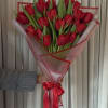 Handheld bouquet of red tulips wrapped in pink paper with a red ribbon