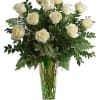 White roses arranged in a tall clear glass vase with greenery