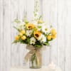 Yellow roses and white daisies in a glass vase with a burlap bow.