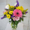 Mixed bouquet of pink, yellow, purple, and white flowers in a glass vase