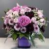 Rounded arrangement of pink roses and purple mums in a purple cube vase