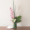 Tall modern arrangement with pink orchids and white roses in a clear cylinder vase