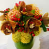 Bouquet with brown orchids, yellow pincushion blooms, and red berries in a green vase