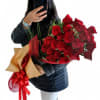 Person holding a large bouquet of red roses wrapped with a red ribbon