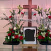 Symmetrical funeral floral display with red and white flowers around a framed photo and cross