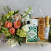 Floral bouquet beside a gift tray with caramels, sea salt, crisps, and olive oil