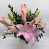 Pink lilies arranged in a white vase with greenery