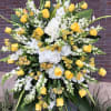 Tall standing spray of yellow roses, white hydrangeas, and white flowers on an easel