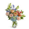 Peach roses, pink carnations, blue hydrangeas, and delphinium in a clear glass vase
