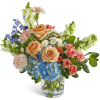 Mixed bouquet of peach roses, blue hydrangea, and assorted blooms in a clear glass vase
