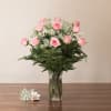 Tall glass vase of light pink roses with white filler flowers and a small matching corsage on the table.