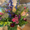 Tall mixed bouquet with blue, pink, yellow, and burgundy flowers in a glass vase