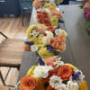 Rows of colorful flower arrangements in clear glass containers on a table