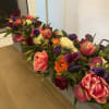 Long low floral arrangement with tulips, roses, calla lilies, and purple blooms