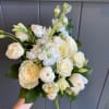 Hand-held bouquet of white roses and other white blooms against a gray paneled background