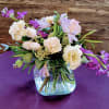 Low arrangement of peach roses and carnations with purple flowers in a clear glass cube vase