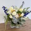 Mixed bouquet in a clear glass vase with blue, white, and yellow flowers