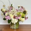 Mixed bouquet of cream, pink, and green flowers in a clear glass vase