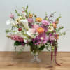 Asymmetrical pastel arrangement with calla lilies, ranunculus, orchids, and mixed blooms in a clear glass vase