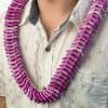 Purple orchid petal lei worn around a person’s neck over a patterned shirt