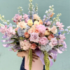 Large pastel bouquet with roses, hydrangeas, and tall blue-white blooms in a pink box
