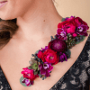 A striking wearable floral piece featuring rich crimson and magenta blooms, layered