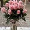 Tall arrangement of pink roses with delicate filler flowers in a glass vase tied with a ribbon