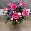 Arrangement of bright pink roses, purple asters, and white spray roses in a clear glass vase