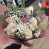 Handheld bouquet of pink and white roses with white filler flowers wrapped in pink paper.
