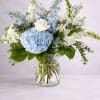 Blue hydrangea and white rose arrangement in a glass vase