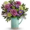 Purple roses and mixed blooms arranged in a turquoise pitcher vase