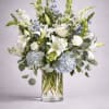 White lilies and blue flowers in a clear glass vase