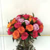 Round bouquet of hot pink, orange, and lavender roses arranged in a clear glass vase.
