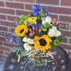 Mixed bouquet with sunflowers, blue flowers, and pale roses in a glass vase