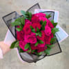 Handheld bouquet of bright pink roses with green foliage in pastel and black wrap