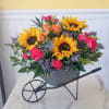 Sunflowers, roses, and carnations arranged in a wheelbarrow planter
