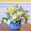 Yellow and white flower arrangement in a blue smiley-face bowl with a butterfly decoration