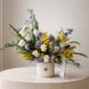 Mixed bouquet of white, yellow, and lavender flowers in a ribbed vase