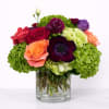 Colorful bouquet of roses, hydrangeas, and a dark anemone in a glass vase