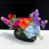 Vivid orange-red roses meet pale blue hydrangea and tall purple stock in