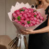 Large bouquet of pink roses wrapped in pale paper with a white ribbon