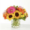 Bright mixed bouquet with sunflowers, gerbera daisies, and orange roses in a glass vase