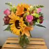 Mixed bouquet of sunflowers, pink roses, and orange lilies in a glass vase