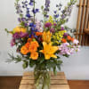 Colorful mixed bouquet in a clear glass vase with orange roses and yellow lilies