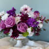 Purple and white floral arrangement in a white pedestal vase