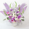 Lavender and purple floral arrangement in a white vase with decorative feathers