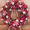 Heart-shaped floral wreath on a wooden easel with pink, red, and white blooms
