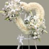 Heart-shaped white floral wreath on a stand with ribbon