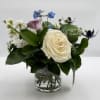 Small arrangement of cream and lavender roses with blue delphinium in a clear glass vase
